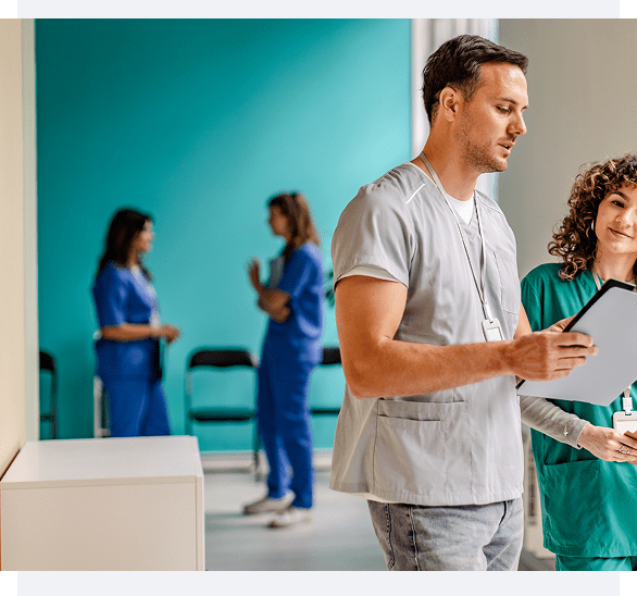 A man and woman discuss paperwork in a healthcare setting with nurses in the background.