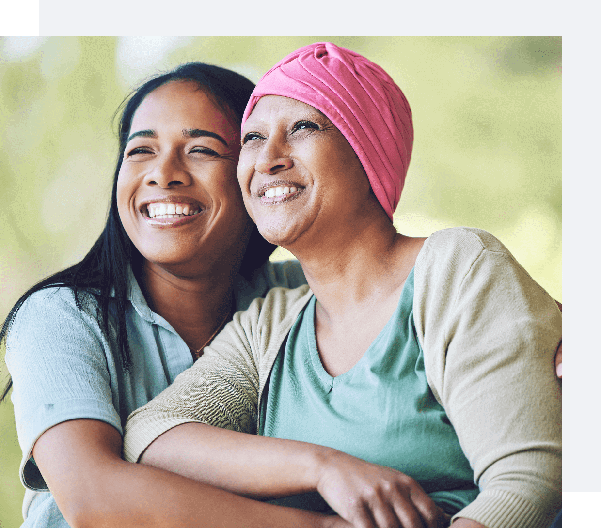 Two women smiling warmly, one wearing a pink headscarf.